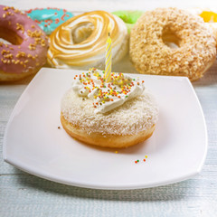 Mini cake with cream with a candle on the background of colorful donuts. Polaroid toning
