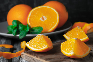 Juicy orange slices. In the background is a plate with orange fruits and mint. Wooden background. Photo taken in a dark style.