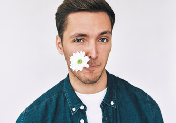 Closeup portrait of attractive man smiling with a flower in mouth posing over white wall. Attractive male model with white flower with balnk copy speca for your promotional text. Mother's day.