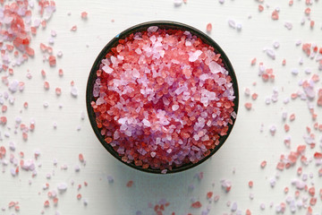 The fragrant and revitalizing sea salt for a bath in a brown bowl stands on a white table in the center, with salt crystals scattered around it.   Close up on a soft natural