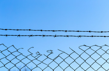 Barbed wire over old wire fence with blue sky