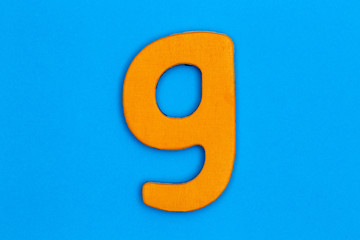Wooden letter g painted orange on a blue background