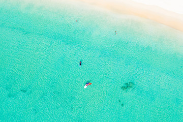 View from above, stunning aerial view of some tourist doing windsurfing and stand up paddle board on a clear and turquoise sea with a beautiful white beach, Phi Phi Island, Thailand.