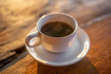 The hot coffee cup with smoke on the wooden table in the restaurant by retro style in the natural light. 