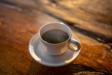 The hot coffee cup with smoke on the wooden table in the restaurant by retro style in the natural light. 