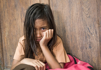 7 or 8 years child in school uniform sitting outdoors on the floor crying sad and depressed holding...