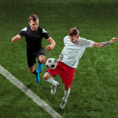 Football player tackling for ball over green grass background. Professional male soccer players in motion at stadium. Fit jumping men in action, jump, movement at game.