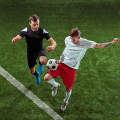 Football player tackling for ball over green grass background. Professional male soccer players in motion at stadium. Fit jumping men in action, jump, movement at game. © master1305