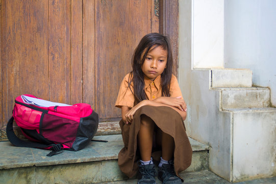 7 or 8 years child in school uniform sitting outdoors sad and depressed with her backpack on the stairs suffering bullying and abuse problem feeling alone and helpless - Powered by Adobe