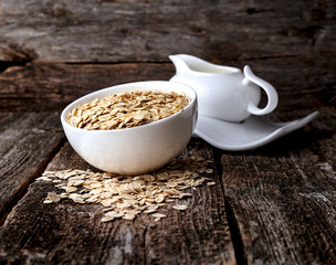 Oatmeal or oat flakes with milk on dark wooden table