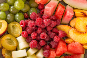 A mixture of their fruit. Peach, grapes, apple, watermelon, melon, raspberry, plum. Juicy and ripe pieces of fruit close-up.