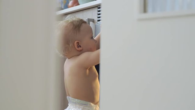 Curious one year old baby girl in diaper exploring the cooker in the kitchen. Home video imitation