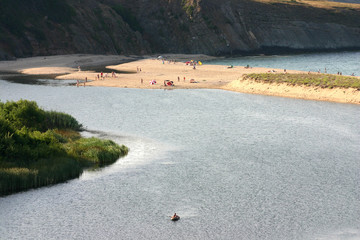 Black Sea, Bulgaria, the estuary of the Veleka River. Tourists on the beach between the river and the sea. A boat swims in the river.