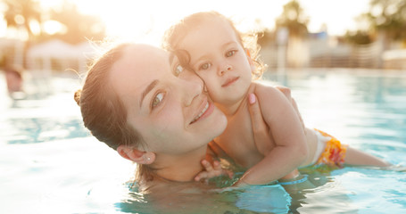 Mom and little daughter are played in the open swimming pool. Family with one child on vacation in...