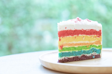 Rainbow cake placed on a wooden plate with nature green bokeh background with natural light.