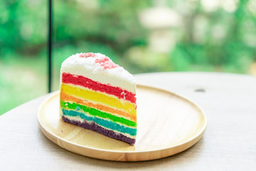 Rainbow cake placed on a wooden plate with nature green bokeh background with natural light.
