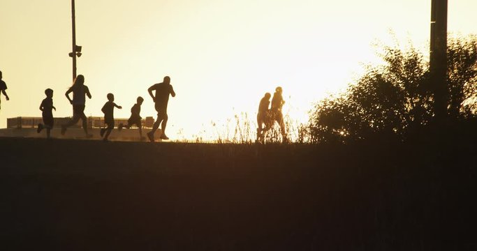 Slow motion Group of runners of all ages, silhouetted against a golden sky