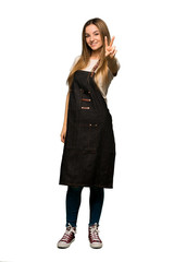 Full body Young woman with apron smiling and showing victory sign on isolated background