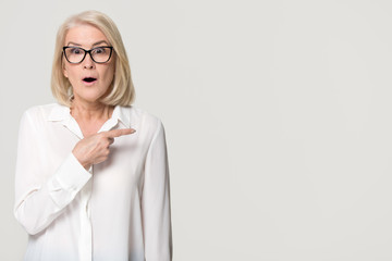 Surprised mature businesswoman pointing finger at copyspace isolated on background