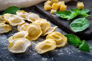 Fresh ravioli with cheese and Basil in flour on wooden background on kitchen table, dark background, close up