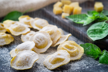Raw ravioli with cheese and Basil sprinkle flour on wooden background on kitchen table, dark background, close up