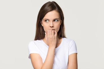 Nervous insecure young woman biting nails isolated on grey background