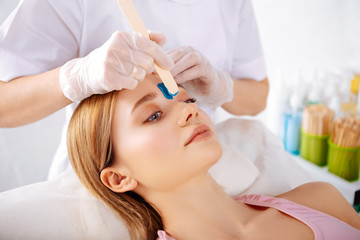 Specialist putting depilatory cream on line between eyebrows