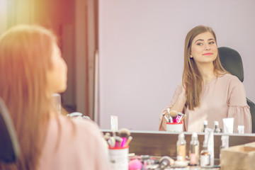 Woman in a beauty salon looks at her reflection in the mirror with lamps and checks hairstyle and makeup