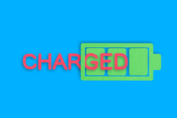Handmade paper icon of full battery with green cells near red word charged in center of blue table. Top view. Technology concept