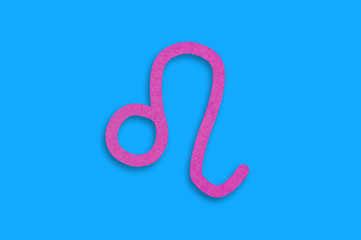 Symbol of astrological sign leo cut out of purple paper in center on blue table. Top view. Horoscope concept