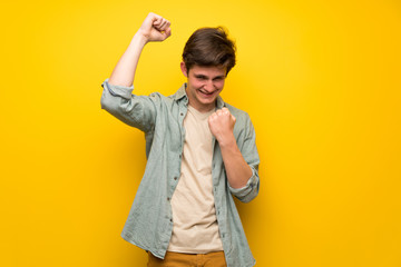 Teenager man over yellow wall celebrating a victory