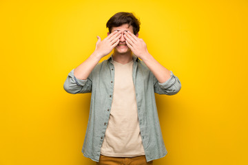 Teenager man over yellow wall covering eyes by hands. Surprised to see what is ahead