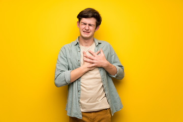 Teenager man over yellow wall having a pain in the heart