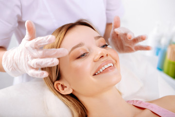 Obraz na płótnie Canvas Cosmetologist making face massage of beautiful smiling client