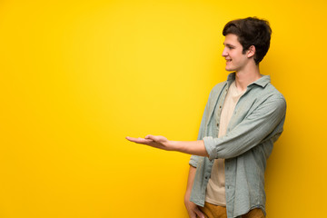 Teenager man over yellow wall presenting an idea while looking smiling towards