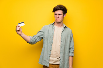 Teenager man over yellow wall taking a credit card without money