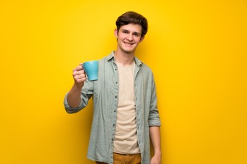 Teenager man over yellow wall holding a hot cup of coffee