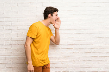 Teenager man over white brick wall shouting with mouth wide open to the lateral