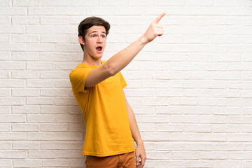 Teenager man over white brick wall pointing away