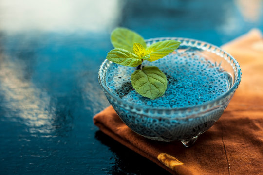 Close up of soaked sabja seeds or falooda seeds or sweet basil seeds in a glass bowl on brown colored napkin on wooden surface with some mint leaves in it.Used in many flavored beverages.