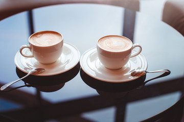 Two cups of cappuccino coffee on a glass table in a cafe with copy space, date concept