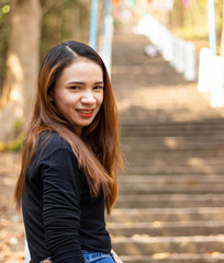Women white skin lovely brown hair a small woman red lips wearing a black shirt wearing a blue gene woman stand  poses photography portrait which has both trees and water in the back in the park.