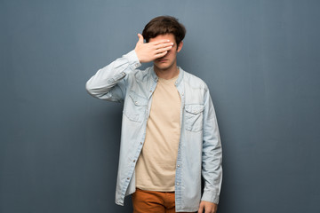 Fototapeta premium Teenager man with jean jacket over grey wall covering eyes by hands. Do not want to see something