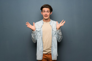 Teenager man with jean jacket over grey wall with shocked facial expression
