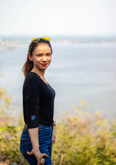 Women white skin lovely brown hair a small woman red lips wearing a black shirt wearing a blue gene woman Wearing yellow glasses stand  poses photography portrait which has water in back in the park.