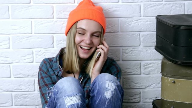 Fashion hipster  stylish young woman in orange hat using smartphone over white brick wall