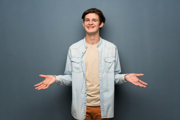 Teenager man with jean jacket over grey wall smiling