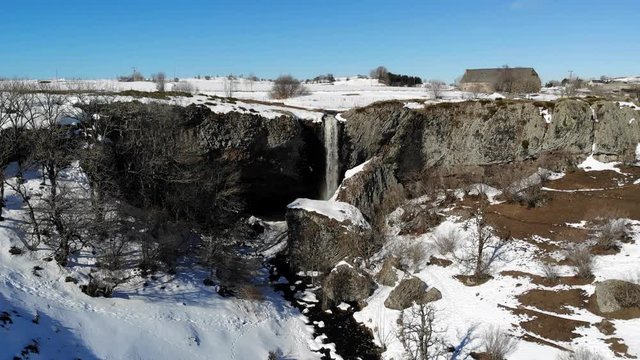 Vol a&eacute;rien vers une cascade qui se jette du haut d'un plateau enneig&eacute;