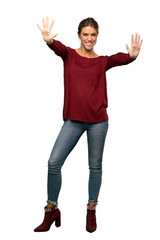 A full-length shot of a Blonde woman counting nine with fingers over isolated white background
