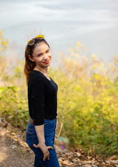 Women white skin lovely brown hair a small woman red lips wearing a black shirt wearing a blue gene woman Wearing yellow glasses stand  poses photography portrait which has water in back in the park.